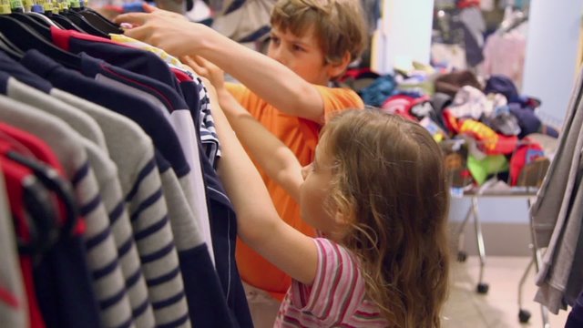 Two kids boy with little girl take and watch shirts in clothes shop