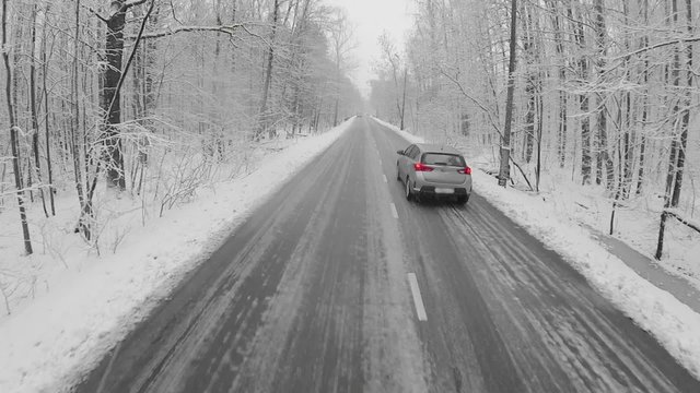 Car drive by icy road in snow-covered forest at winter