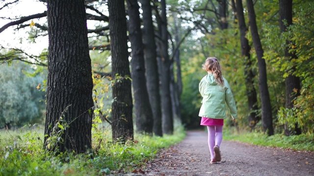 Cute little girl walk away on footpath through the forest 