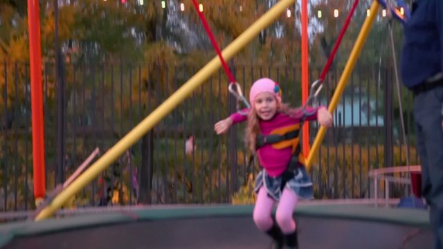 girl jumps on trampoline with rope support and man helps her