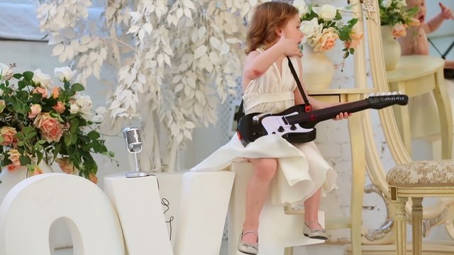 Beautiful little girl in white dress sings and plays guitar