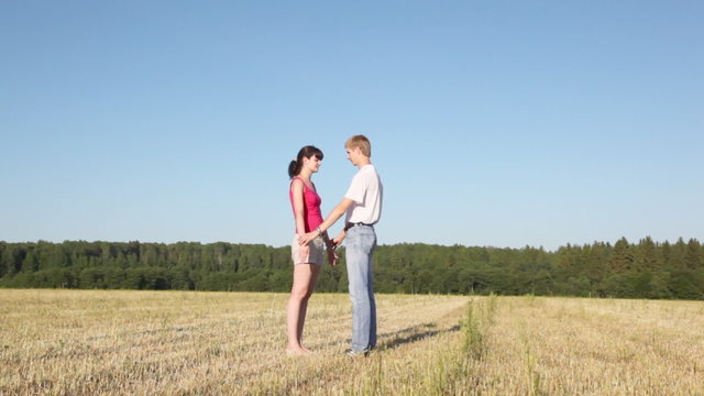 girl stands having placed hands in field, guy stands nearby