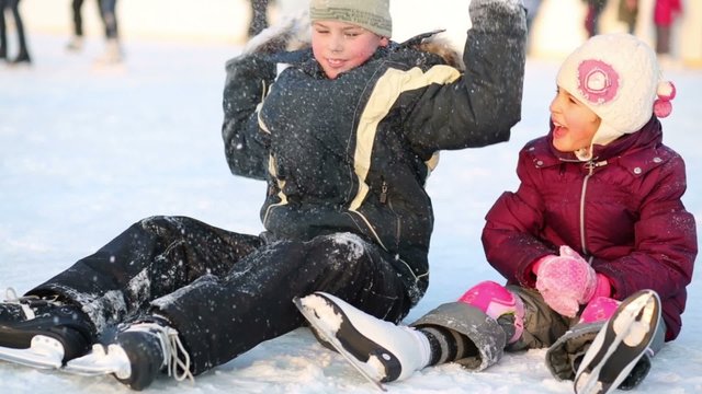 Happy boy and girl sit on ice after learning to skate at winter