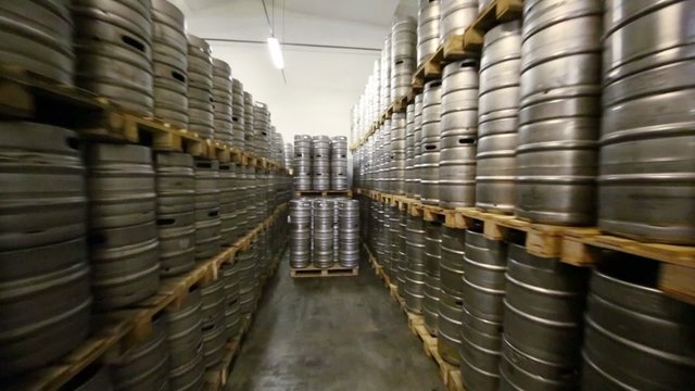 Movement along high rows of metal beer kegs in warehouse