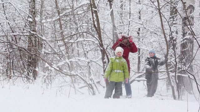Mother with her kids shake branches for make snowfall in park - Powered by Adobe