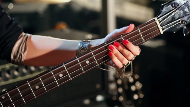 Girls hand with chains hold chords on bass guitar, closeup