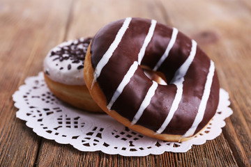 Delicious donuts with icing on lace doily on wooden background