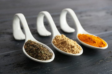 Different kinds of spices in spoons on wooden background