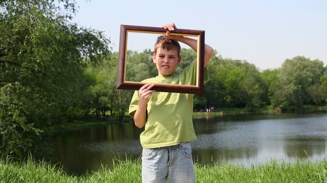 Young boy holds picture frame and rotates it near near face