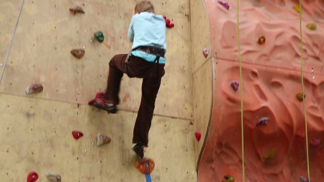 Boy descends down from steep wall at climbing gym hall