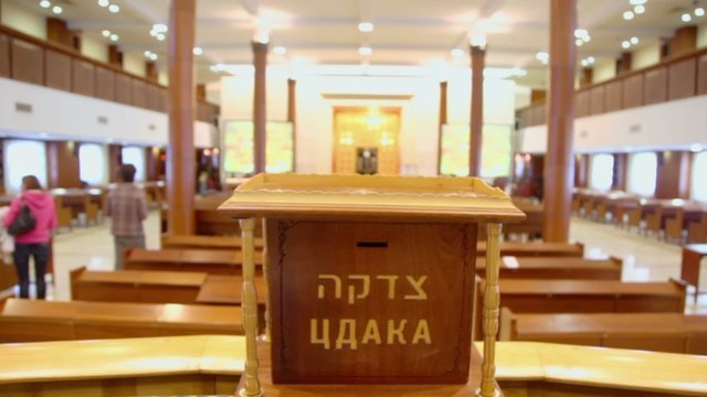 people walk in synagogue with jewish wooden box for charity