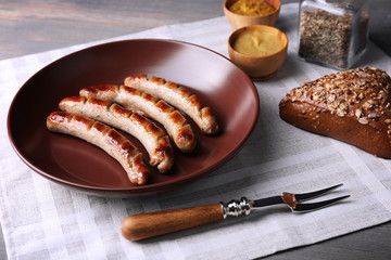 Grilled sausages on plate with bread on table close up
