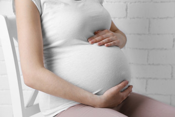 Young pregnant woman sitting on chair on light background