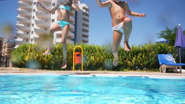 Two children girlfriends run and jump into the pool near hotel