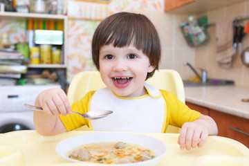 Lovely little boy eating soup with meat balls