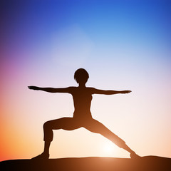 Fototapeta na wymiar Woman in worrior yoga pose meditating at sunset. Zen