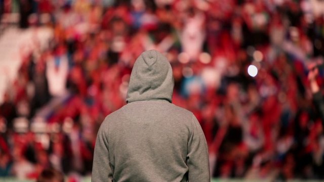 Football fan in hood stand against tribunes with crowd