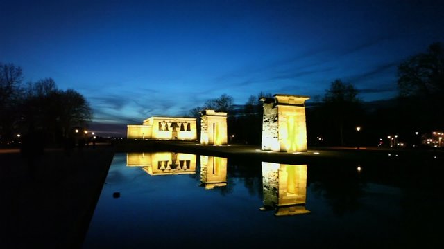 Tourists walk near pond and Temple of Debod with illumination