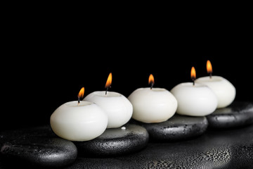 Obraz na płótnie Canvas spa concept of white candles on zen stones with water dew black