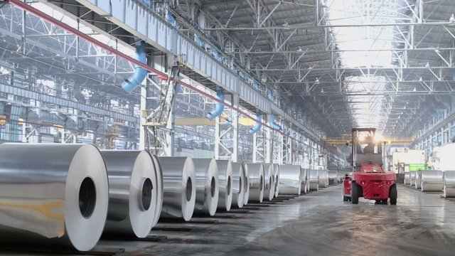 Loader machine rides by storage of aluminum rolls at workshop