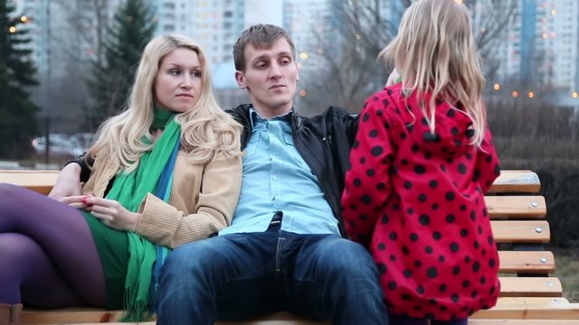 Young couple sit on bench and father checks clothes