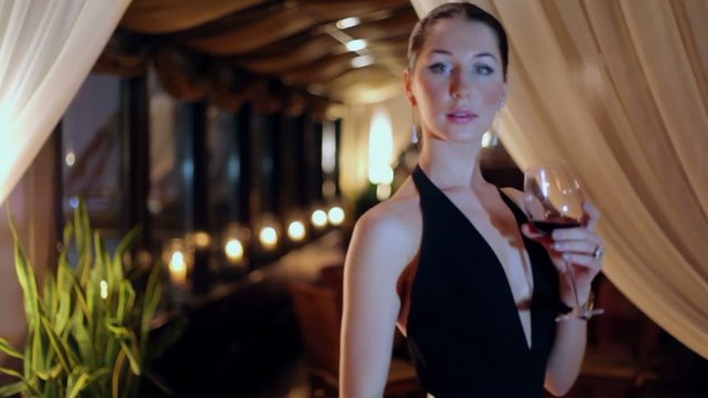 Woman turns around, drinks wine from glass, then she walks away