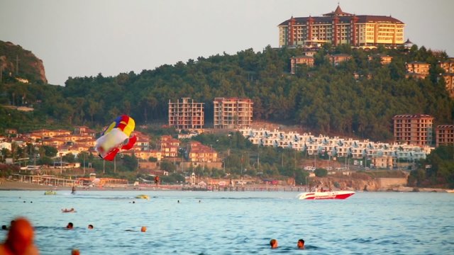 People rise up on parasail attraction at beach of Antalya