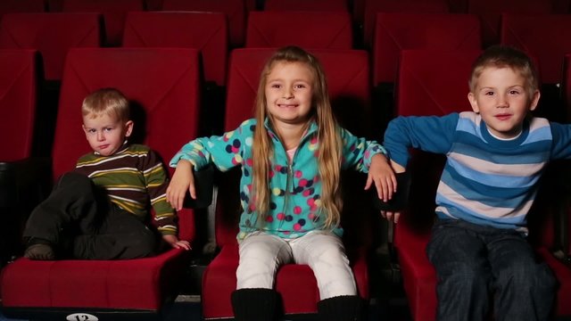 Three small children together watching a movie at the cinema