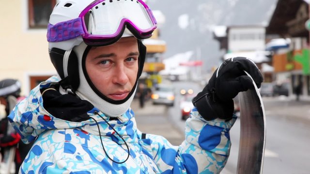 Snowboarder stands on street near road and moving cars