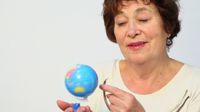 Senior woman holds earth miniature and spins it, closeup
