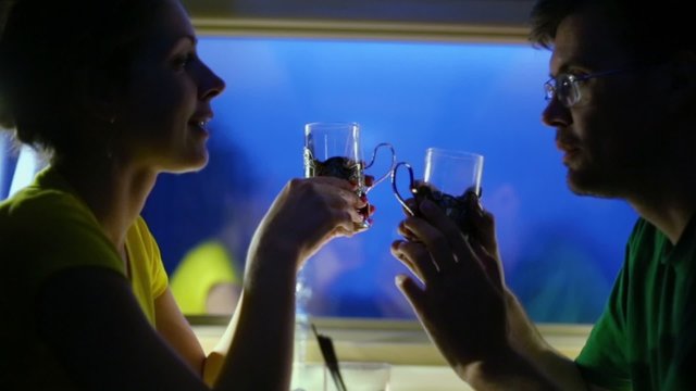Couple drink tea and talk in dark compartment of train