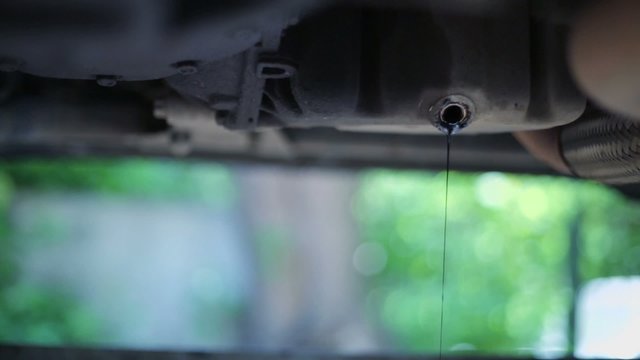 Thin jet of dark oil which pours out from car reservoir hole