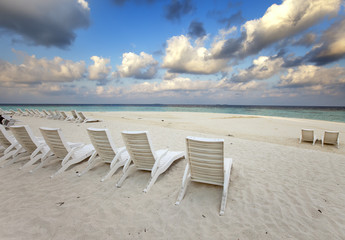 Empty beach chairs on sand by the sea at sunrise