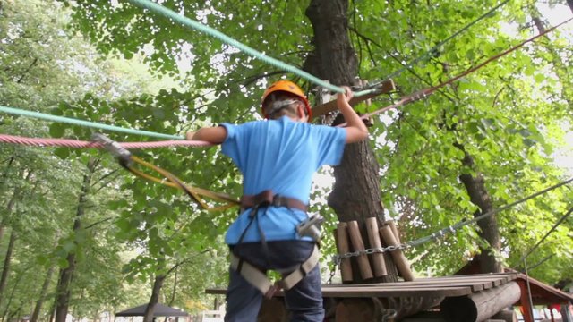 Boy walks by pendant path to platform on tree at rope park