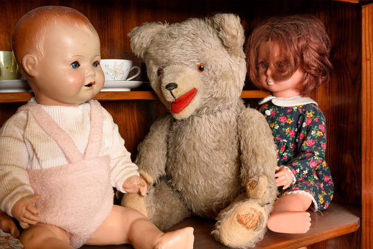 Antique teddy with dolls sitting in a cabinet