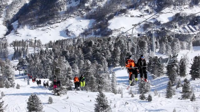 Skiers rise in chairlift over valley to mountain top to ski 