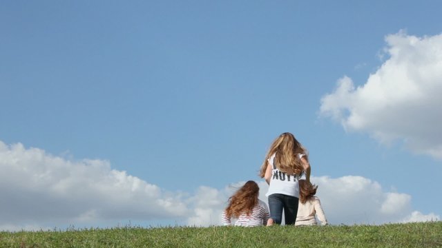 Three young girls run away on grass hill at sunny summer day