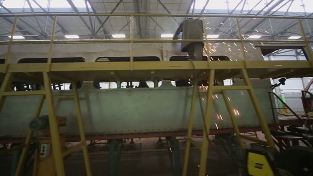 Worker stands on falsework and weld train wagon at workshop