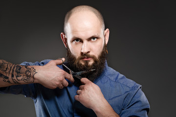 Portrait of a bearded man grooming his beard with scissors