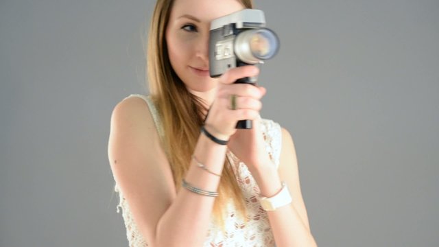 Woman with vintage camera filming against grey background. 
