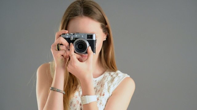 Woman with vintage camera filming against grey background. 