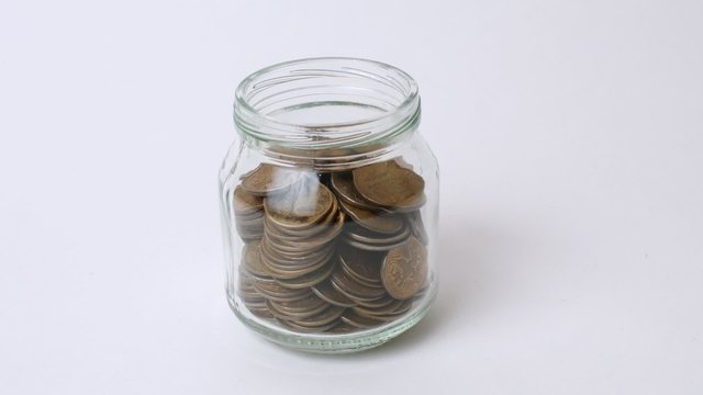 Lots of coins in a jar on white. Stop motion
