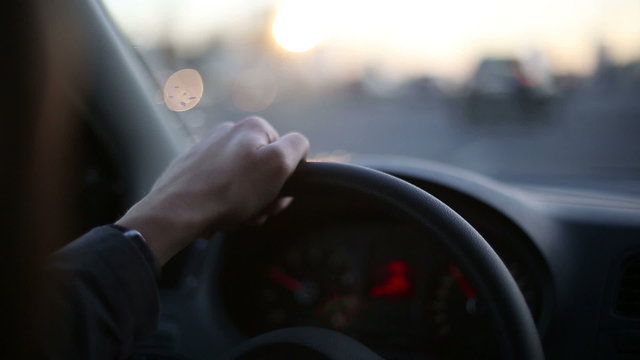 Man's hand is driving car at sunset