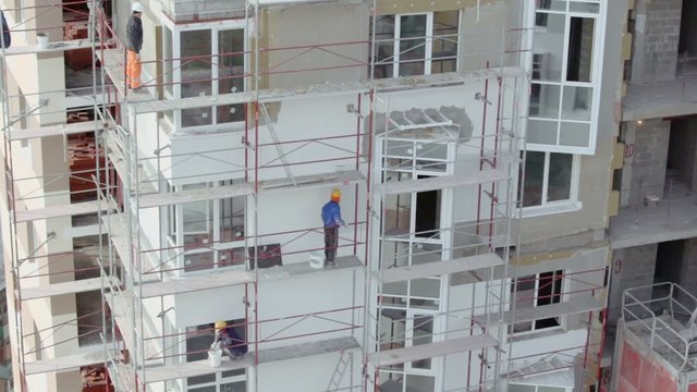 Builders stand on scaffold and make thermoinsulation of walls