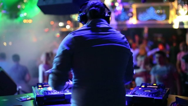 Rear view of DJ which dance at his workplace during party