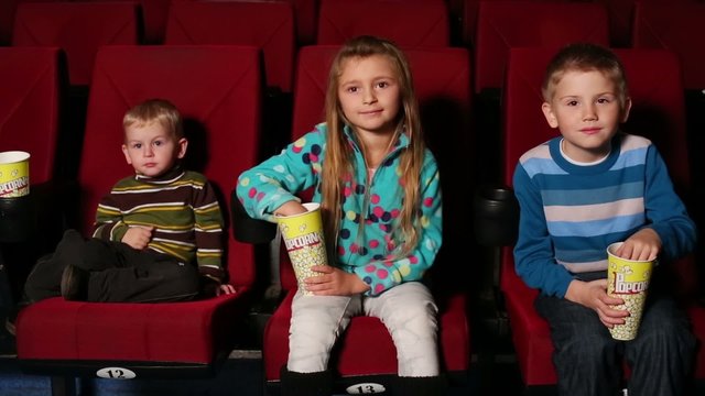 children with popcorn in hand watching a movie at the cinema