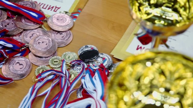 Medals with ribbons, diplomas and cups lay on table