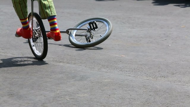 Feet of three clowns riding on unicycles on holiday outdoor