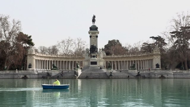 Tourist sails on boat near monument to Alfonso XII at pond