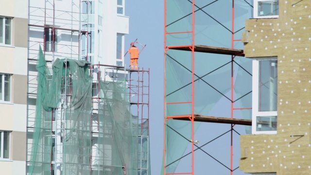 Labourer in orange uniform stands on falsework of dwelling house
